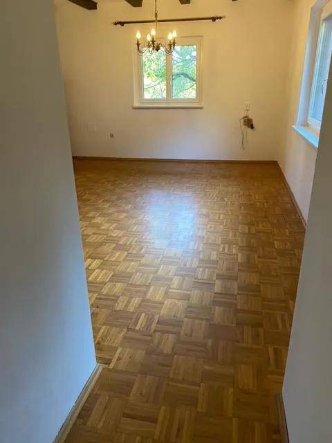 Geräumiges Wohnzimmer mit Parkettboden, Fenster und einem klassischen Kronleuchter.