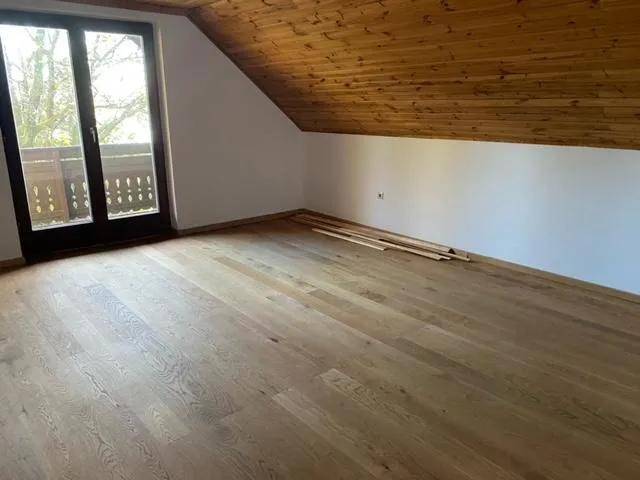 Helles Schlafzimmer im Dachgeschoss mit Holzboden, schräger Holzdecke und Zugang zum Balkon.