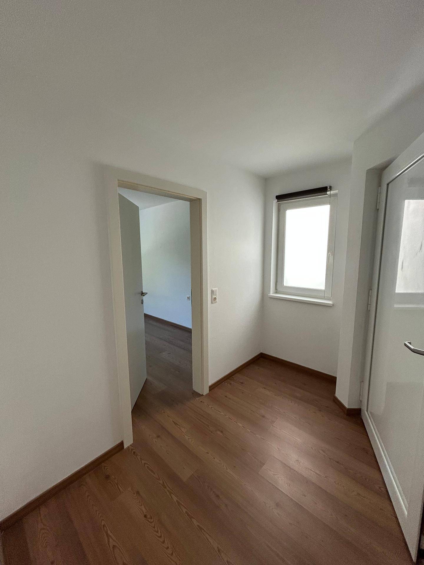 Heller Flur mit Holzboden und weiß gestrichenen Wänden, der zu weiteren Räumen führt.