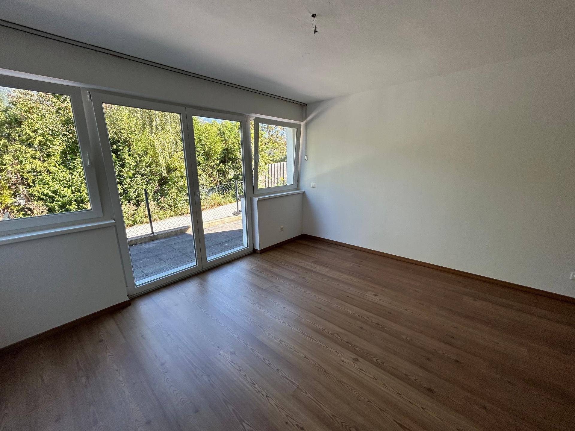 Helles Wohnzimmer mit Holzboden und breiter Glasfront, die auf eine Terrasse führt.