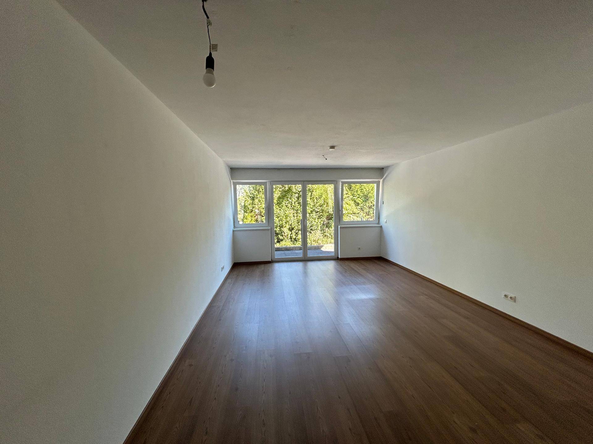 Geräumiges Wohnzimmer mit Holzboden und großen Fenstern mit Zugang zur Terrasse.