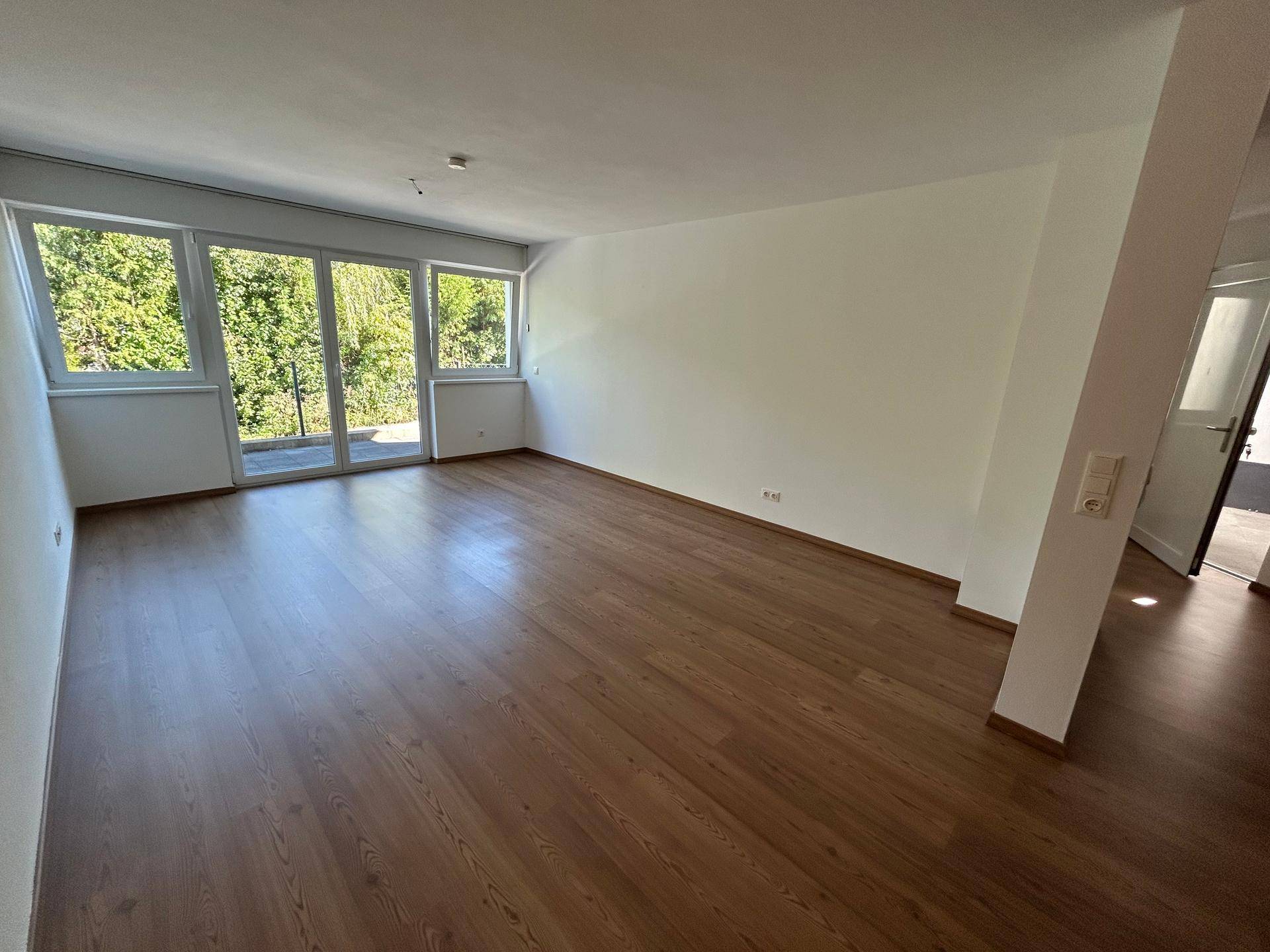 Großzügiger Wohnraum mit Holzboden und viel Tageslicht durch die breite Fensterfront.