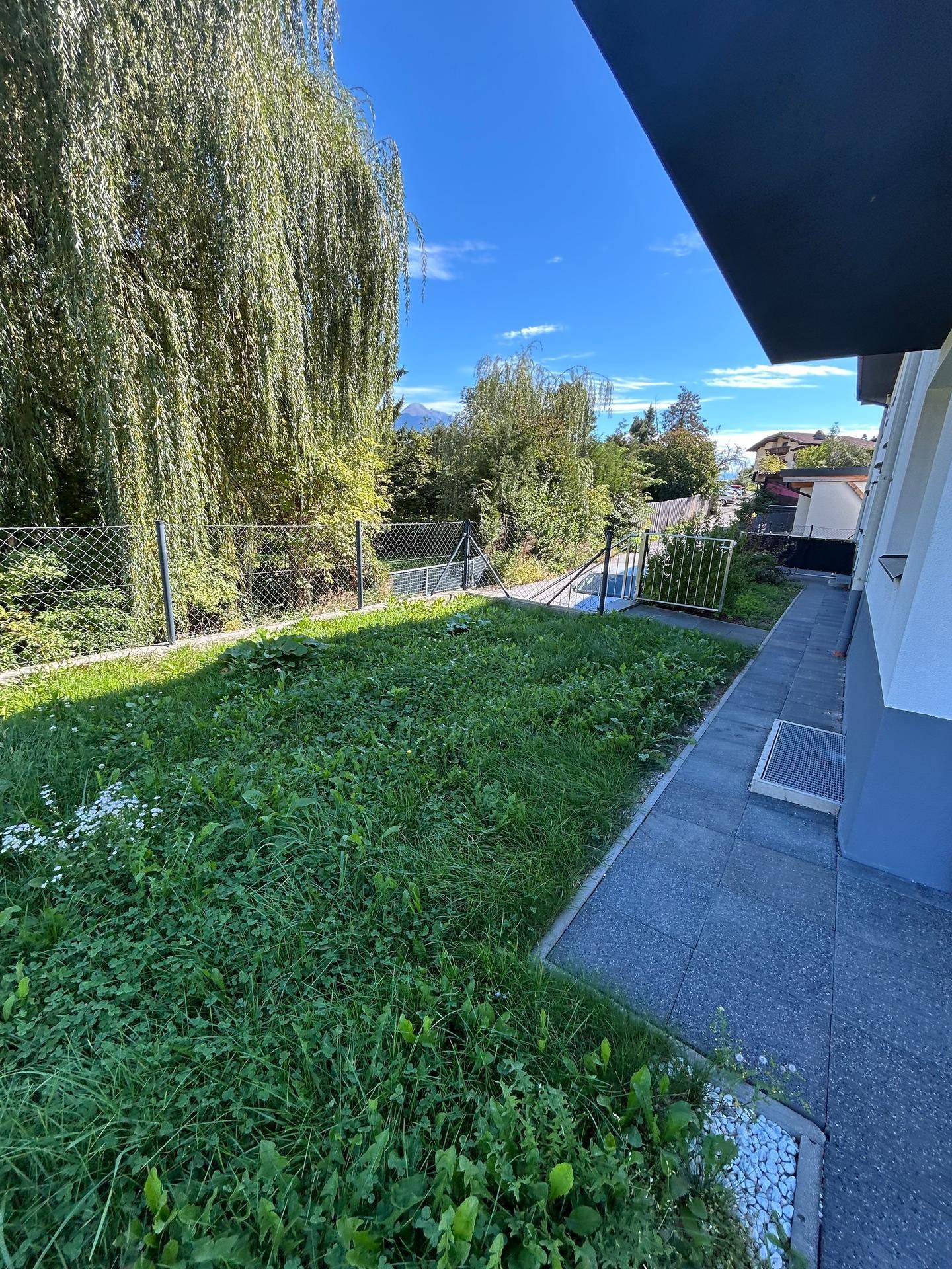 Grüner Gartenbereich neben dem Gebäude mit Zaun und Zugang zu einem Weg.