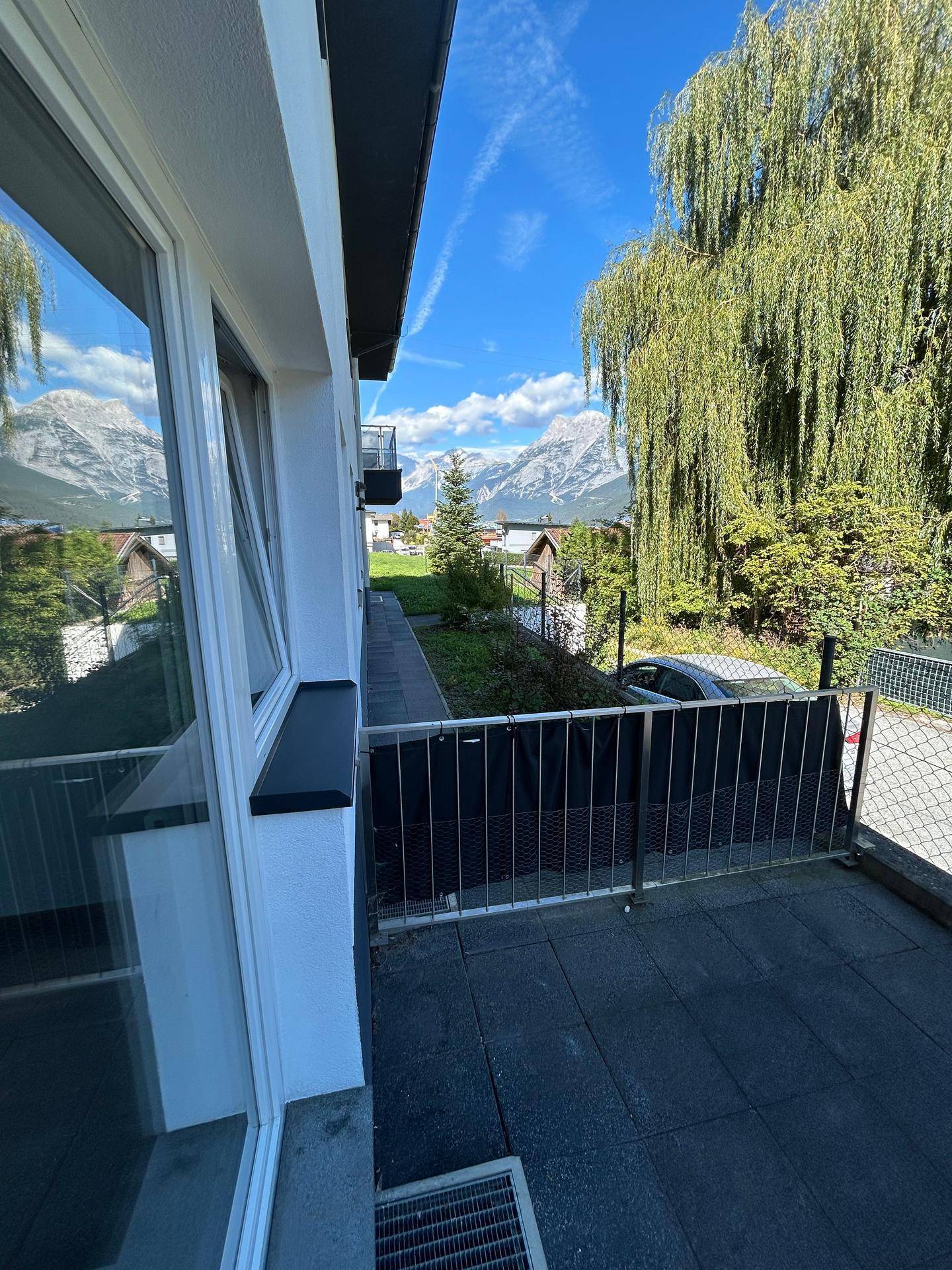 Terrasse mit Bergblick und seitlichem Zugang zum Gartenbereich, umgeben von Bäumen.