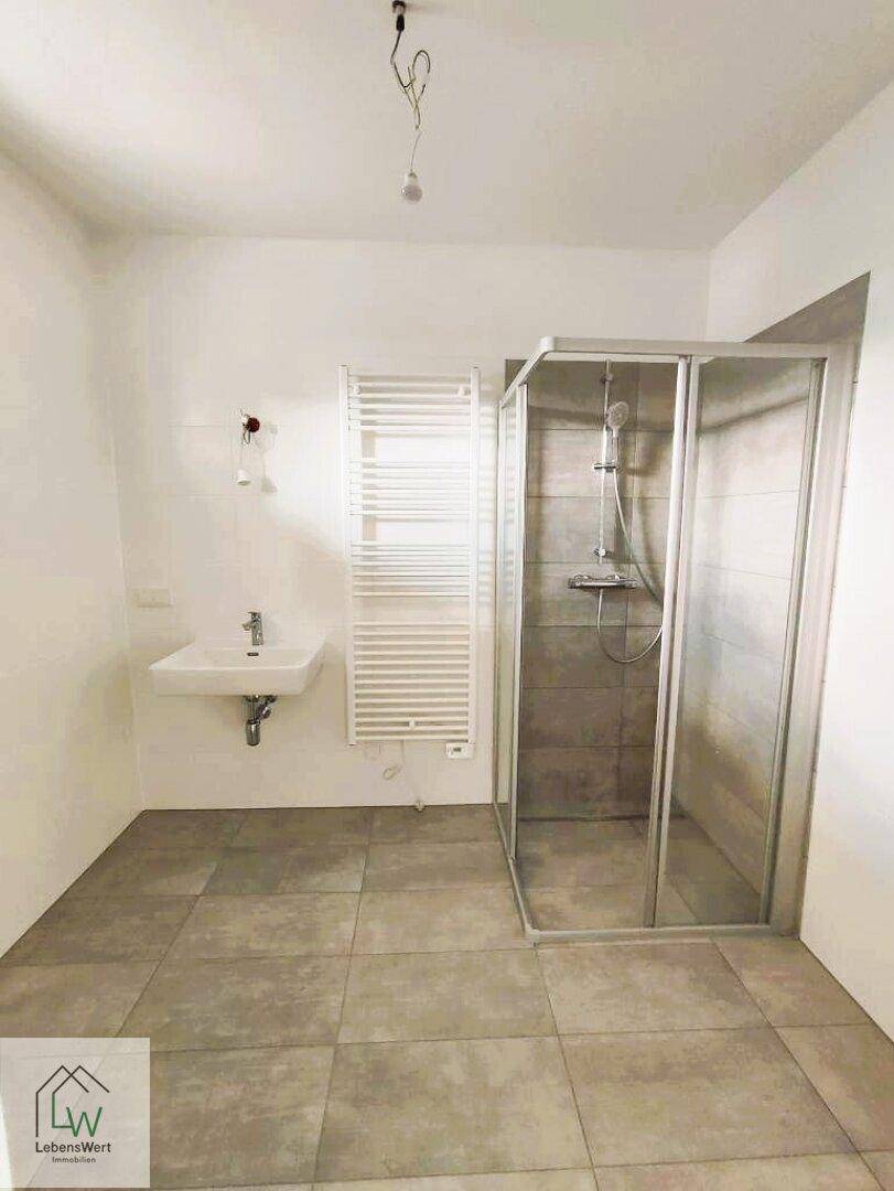 Modernes Badezimmer mit Duschkabine, Waschbecken und beheiztem Handtuchhalter in neutralen Farben.