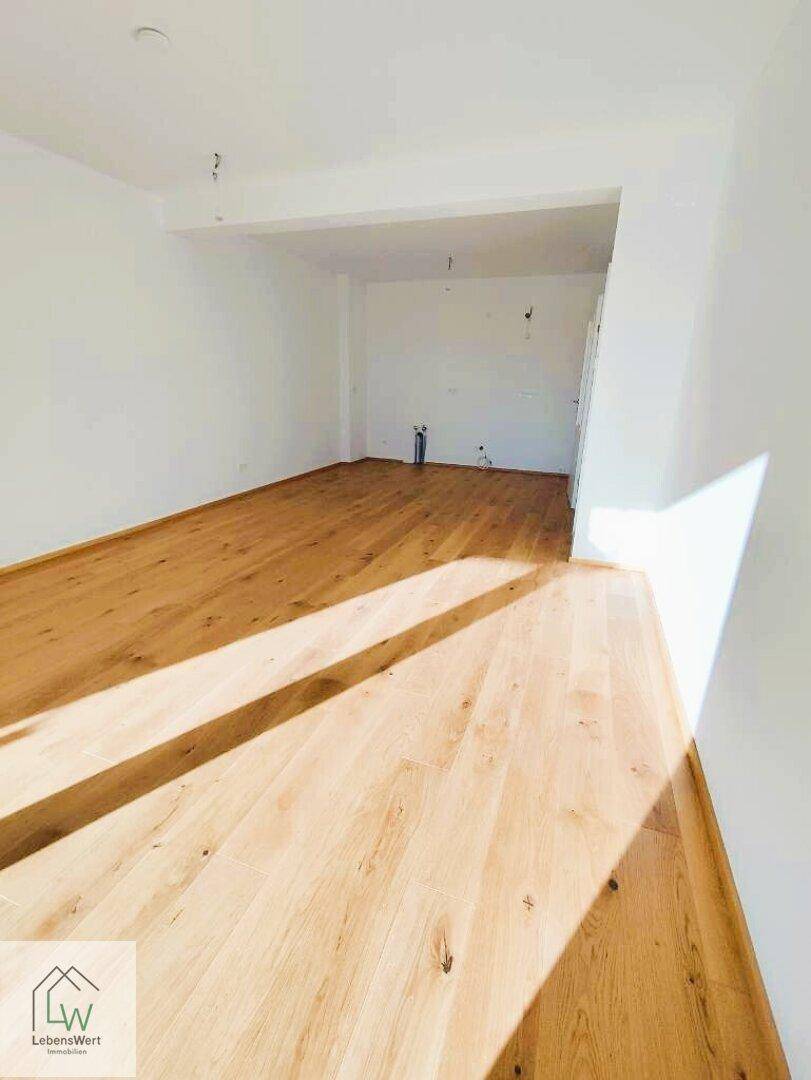 Heller, unmöblierter Raum mit neuem Holzparkettboden und vorbereiteten Anschlüssen für eine Küche.