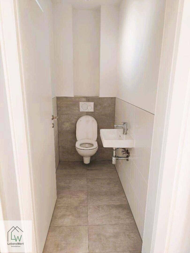 Kleines Gäste-WC mit wandhängender Toilette und kompaktem Waschbecken, ideal für Besucher.