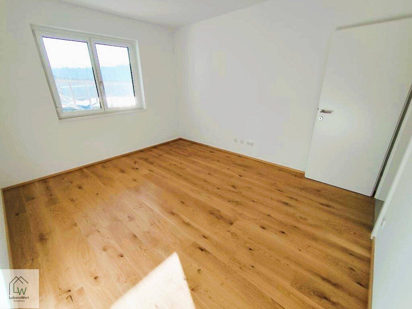 Helles Schlafzimmer mit neuem Holzparkettboden und großem Fenster für viel Tageslicht.