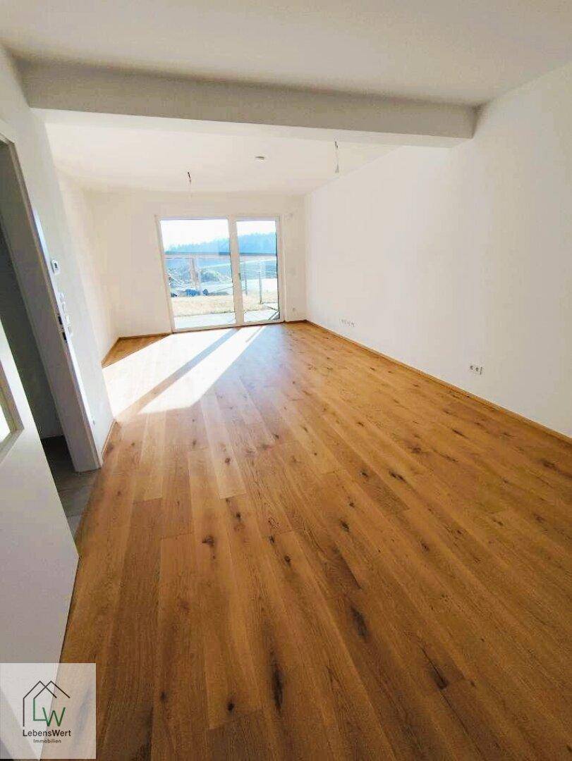 Lichtdurchfluteter Wohnbereich mit Holzparkettboden und direktem Zugang zu einer zukünftigen Terrasse.