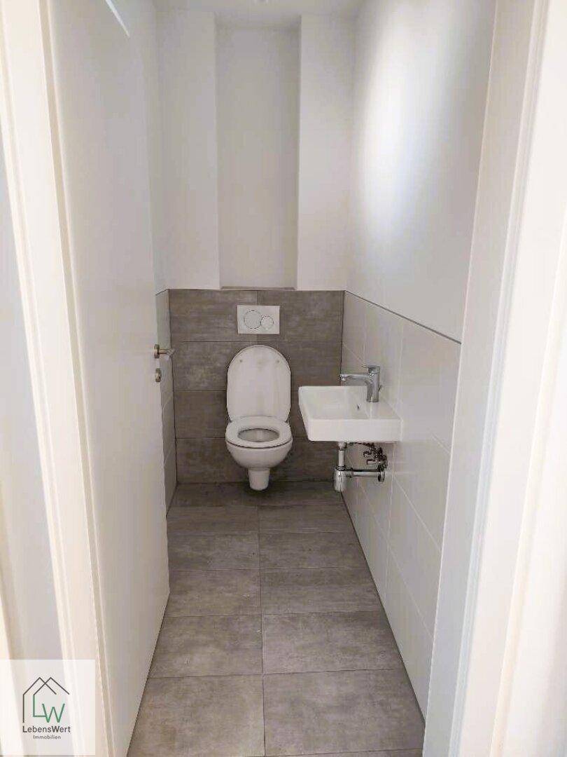 Kleines Gäste-WC mit Wand-WC, kleinem Waschbecken und Fliesenboden.