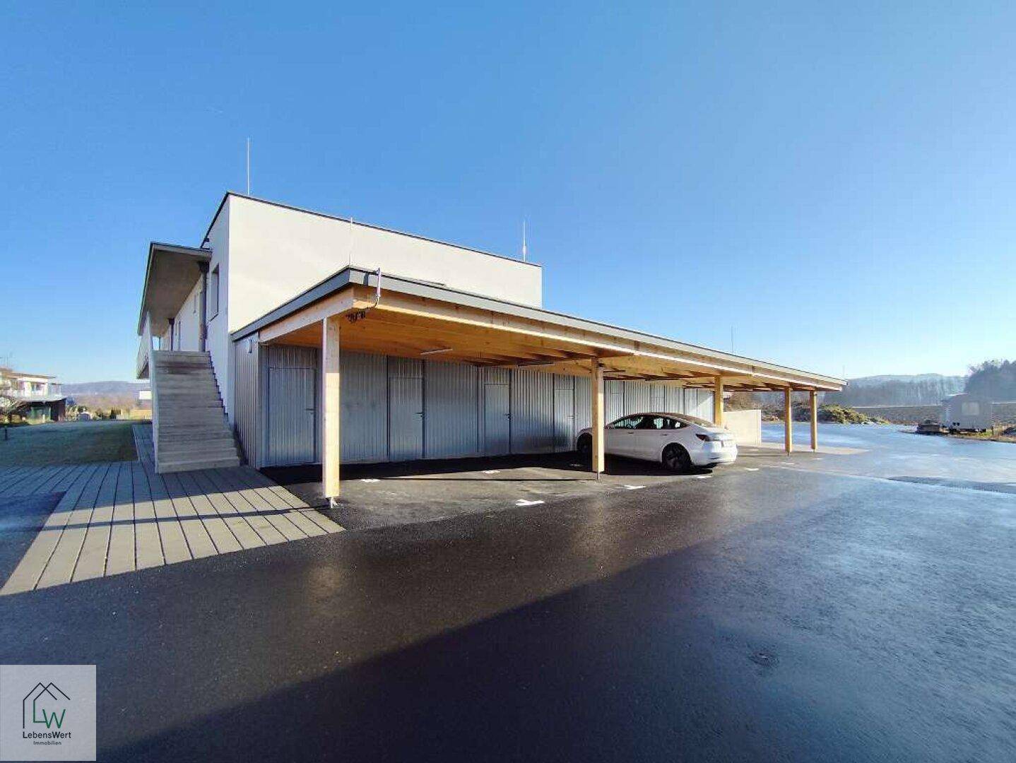 Überdachter Carport-Bereich mit Parkplätzen und abschließbaren Abstellräumen.