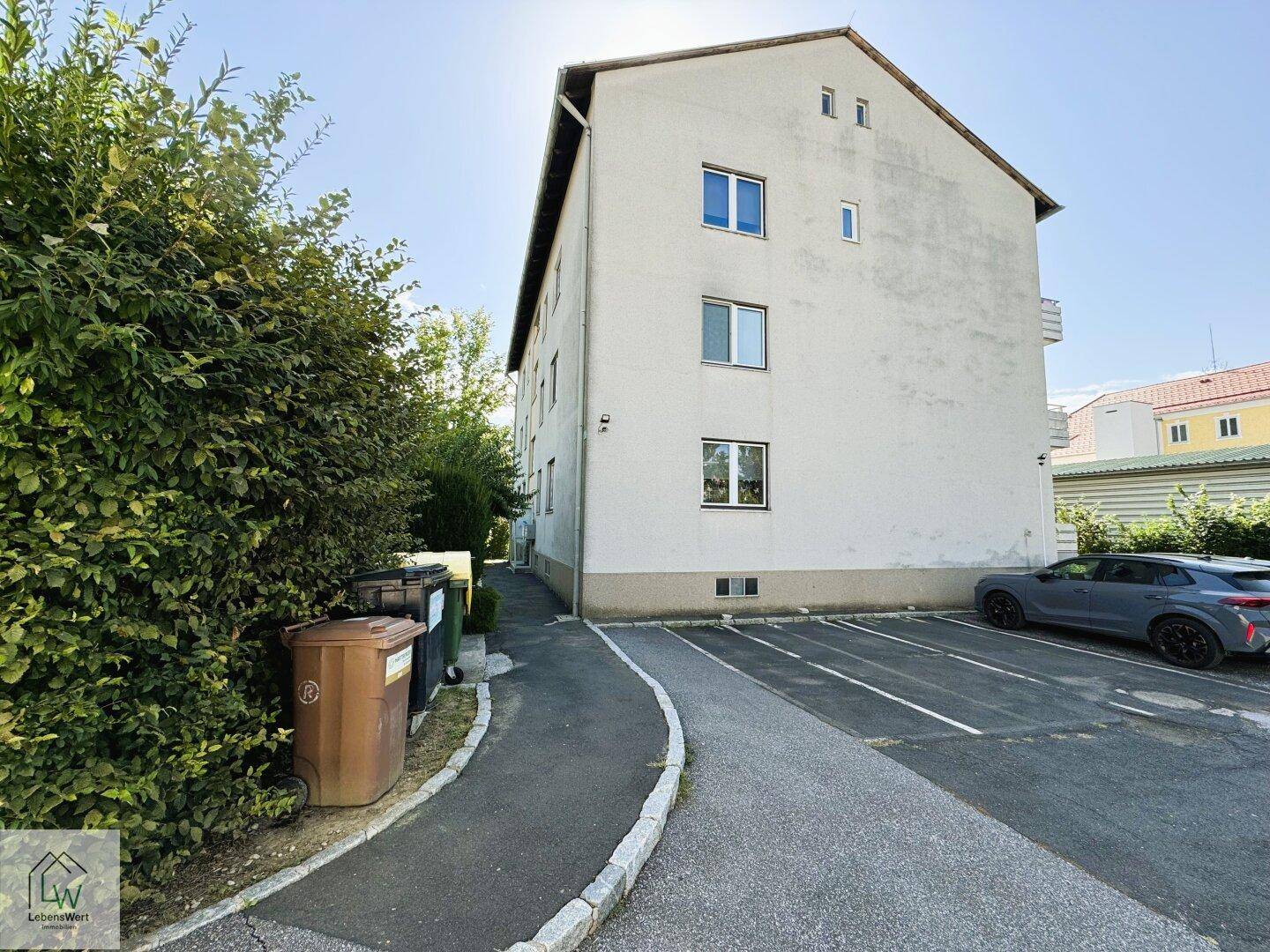 Seitenansicht des Mehrfamilienhauses mit Parkplätzen und gepflegter Grünanlage.