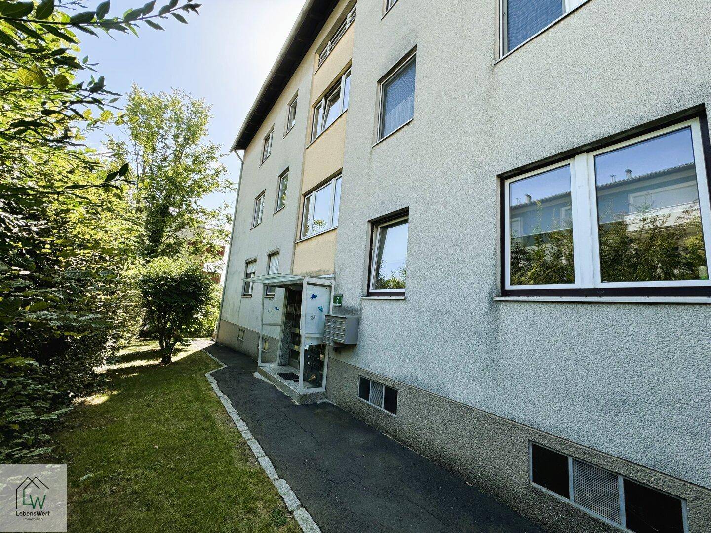 Eingangsbereich des Wohnhauses mit Zugangsweg und umgebender Grünfläche.