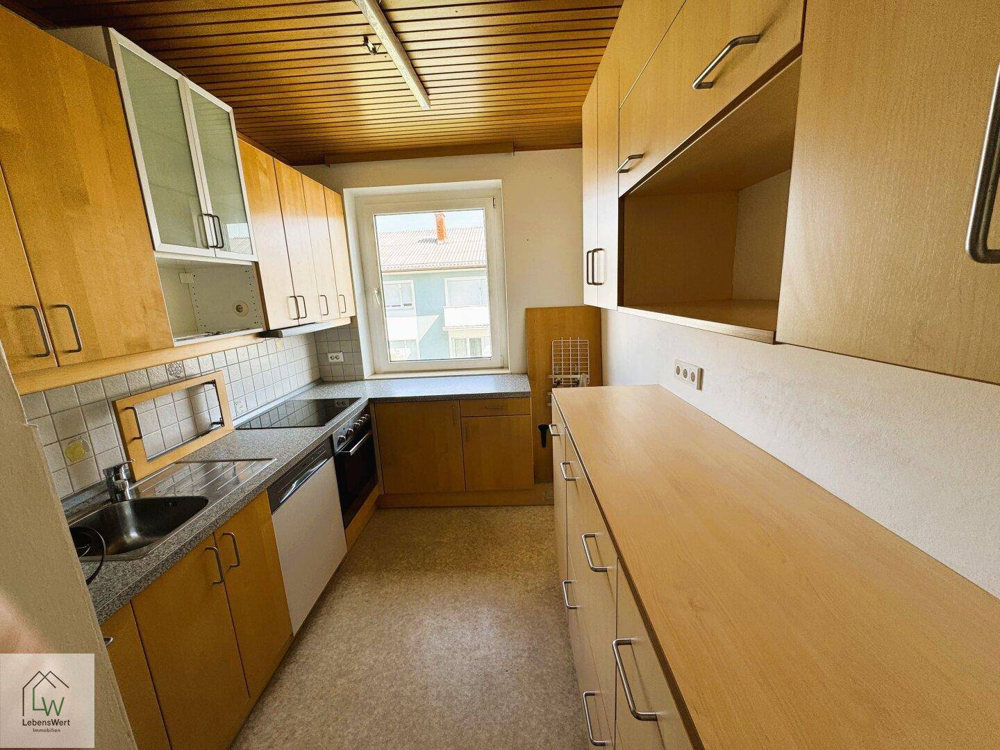 Funktionale Küche mit Holzschränken, Fenster und integrierten Geräten.