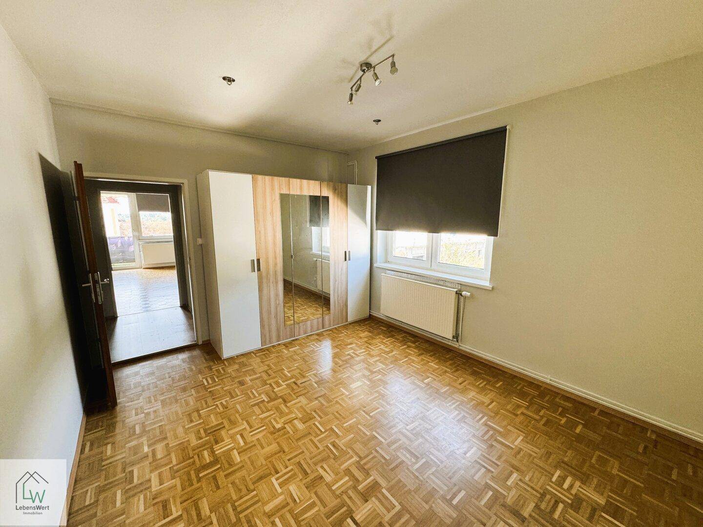 Schlafzimmer mit Parkettboden, großem Kleiderschrank und Fenster für natürliches Licht.