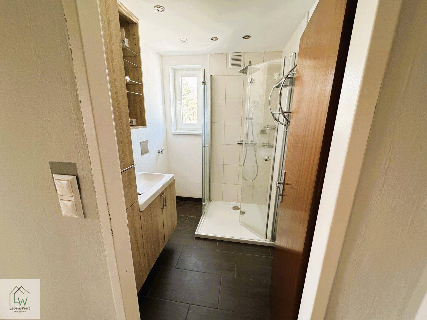 Modernes Badezimmer mit Dusche, Waschbecken und Fenster für gute Belüftung.