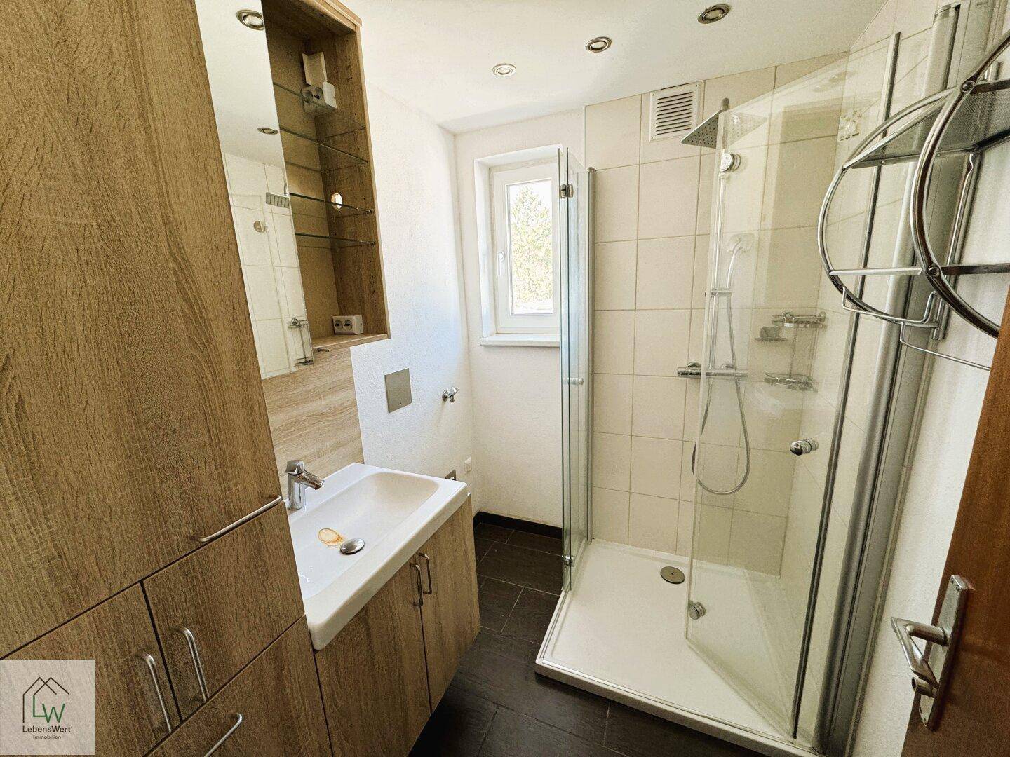 Helles Badezimmer mit Duschkabine, Holzwaschtisch und Spiegelschrank.