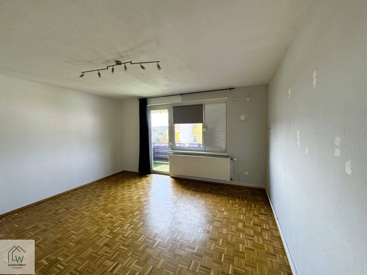 Geräumiges Wohnzimmer mit Parkettboden und Zugang zu einem Balkon oder einer Terrasse.