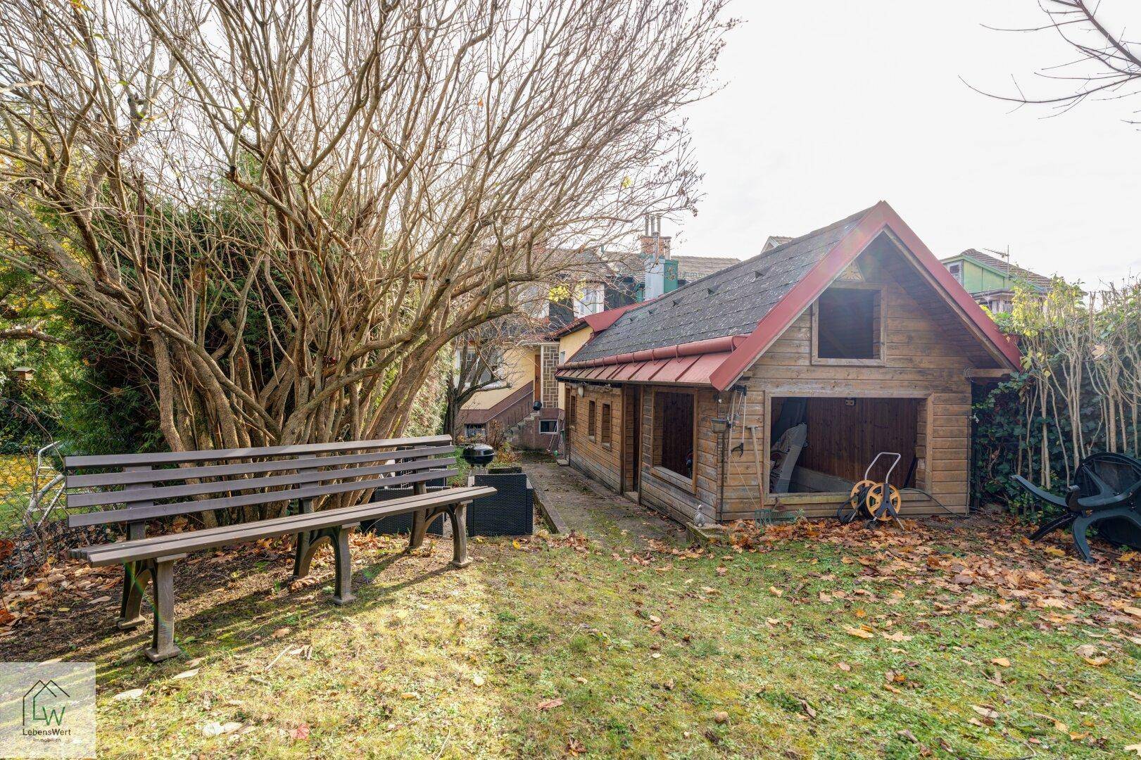 Gartenbereich mit einer Holzbank, Grill und einem kleinen Holzschuppen im Hintergrund.