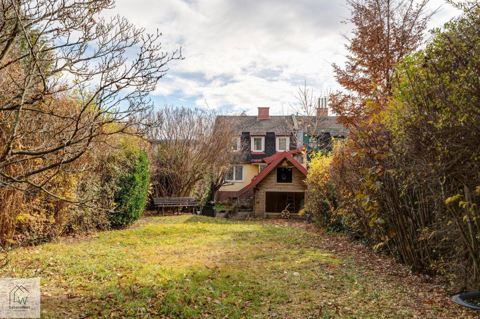Großer Gartenbereich mit Rasenfläche und altem Baumbestand, Blick auf das Haus im Hintergrund.