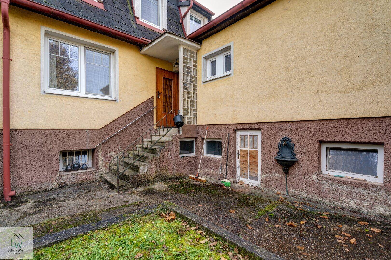Hauseingang mit Steintreppe und Zugang zum Kellergeschoss, umgeben von einer gelben Fassade.