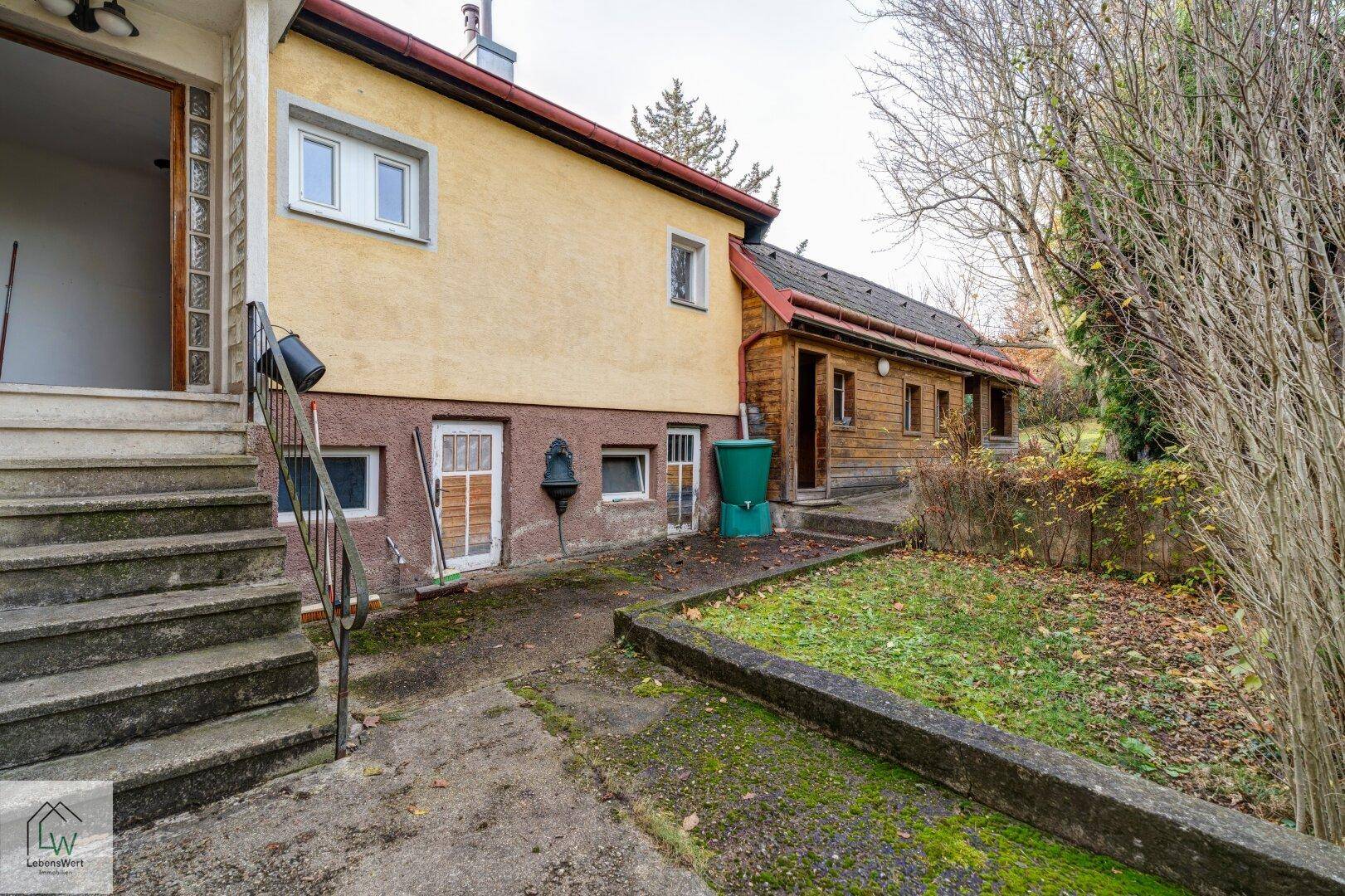 Seitenansicht des Hauses mit Zugang zum Garten und einem angrenzenden Holzschuppen.