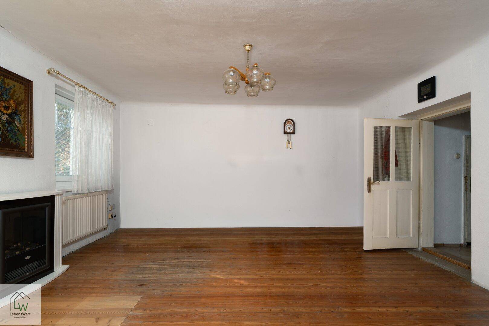 Geräumiges Wohnzimmer mit Holzdielenboden, Kamin und einem Fenster mit Tageslicht.