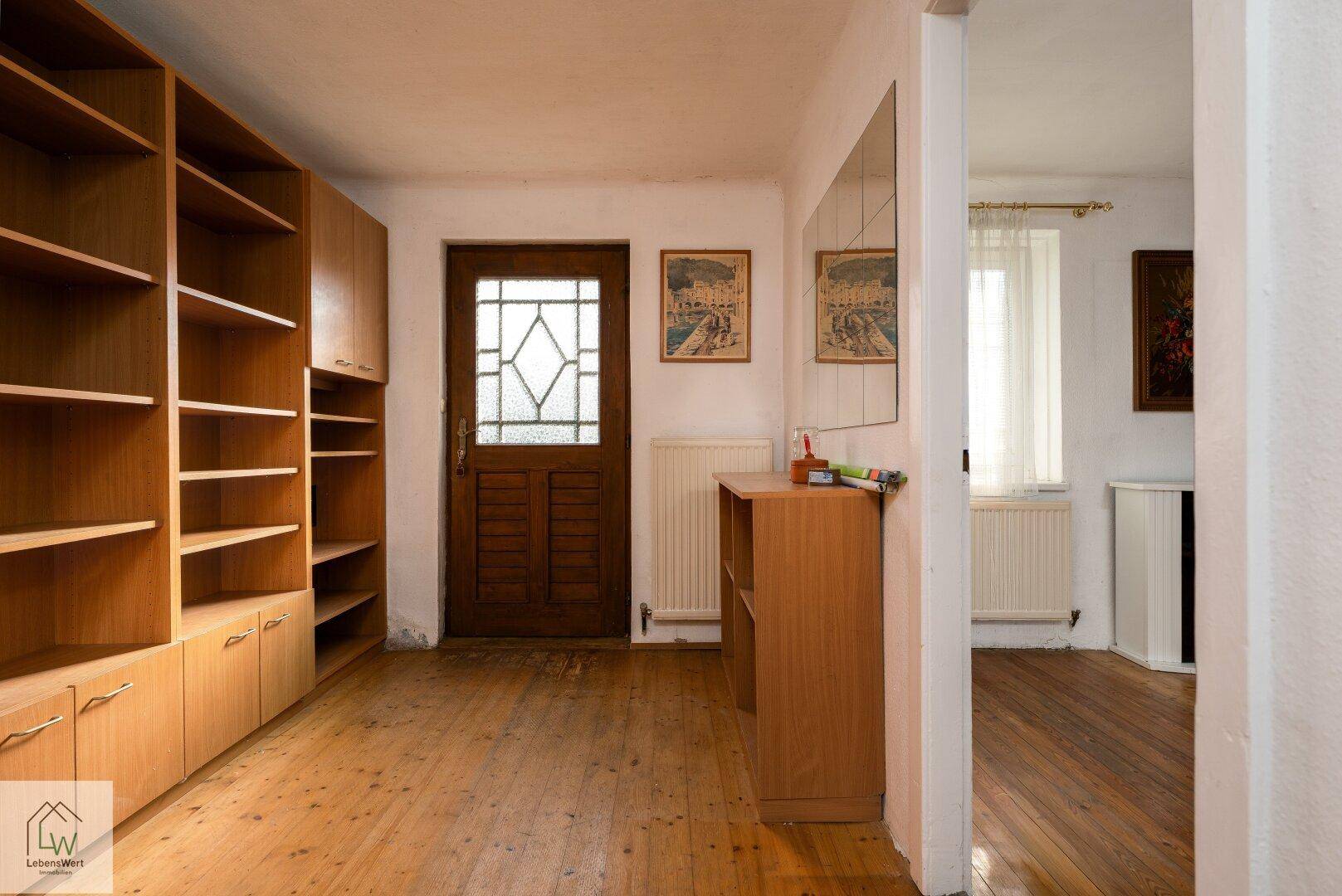 Flur mit Holzdielenboden, Einbauregalen und einer Holztür mit Glaseinsatz.