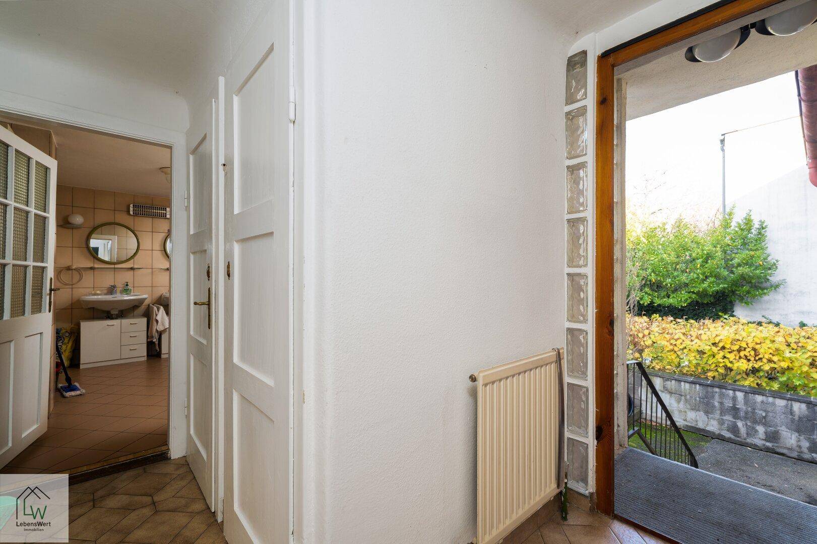Eingangsbereich mit Fliesenboden und Blick auf das Badezimmer und den Außenbereich.