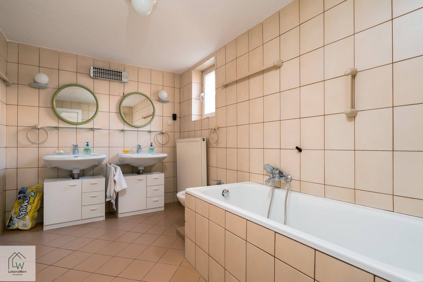 Geräumiges Badezimmer mit beigefarbenen Fliesen, Doppelwaschbecken und Badewanne.