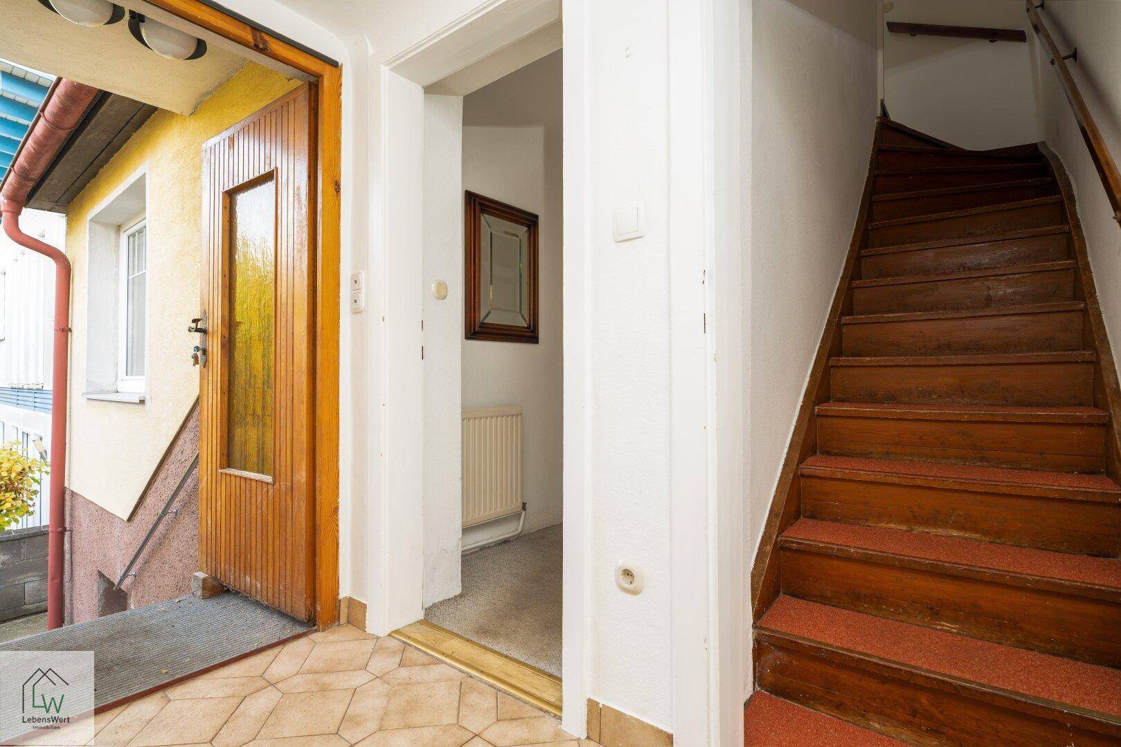 Eingangsbereich mit Fliesenboden und Holztreppe, die in die oberen Stockwerke führt.