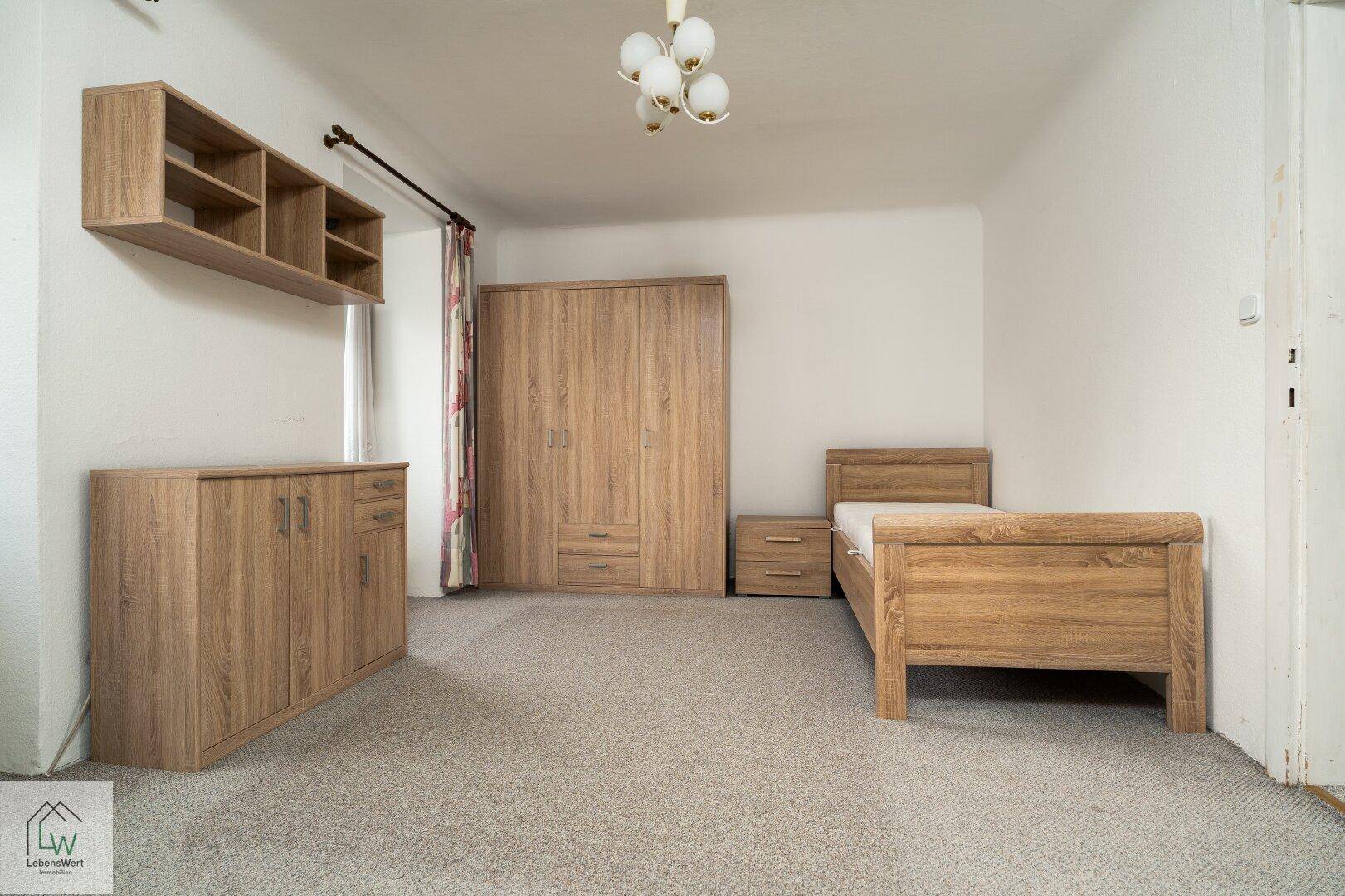 Schlafzimmer mit Teppichboden und Holzmöbeln, darunter Bett und Kleiderschrank.