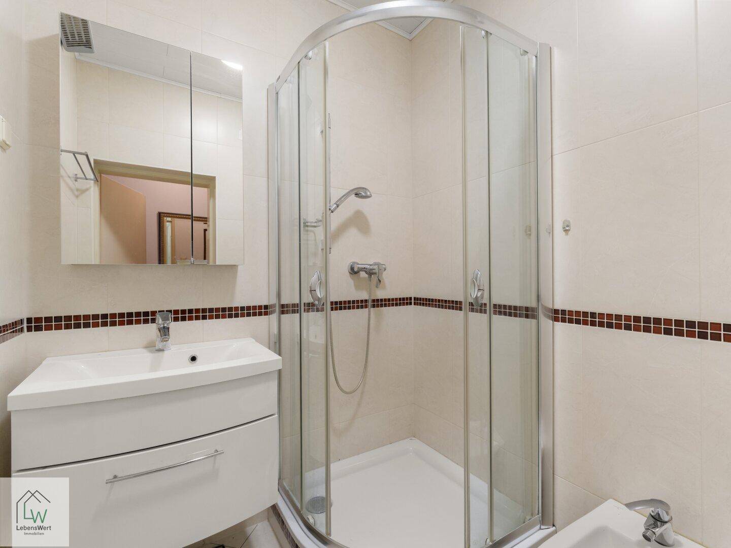 Badezimmer mit Eckduschkabine, Einzelwaschbecken und Bidet, in hellen Fliesen gehalten.