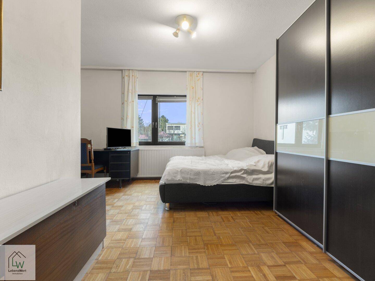 Schlafzimmer mit Parkettboden, großem Kleiderschrank und Blick ins Grüne.