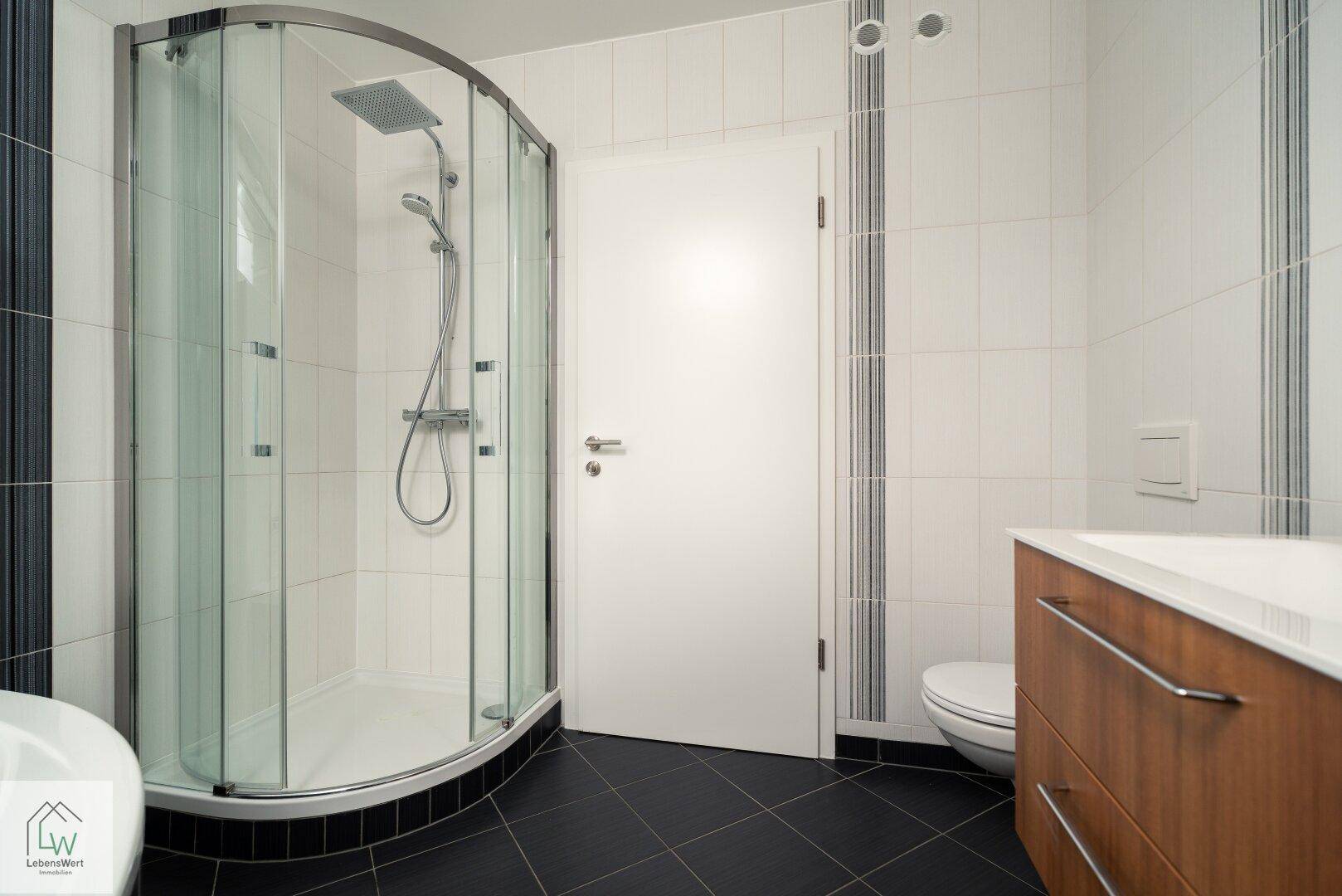 Badezimmer mit moderner Duschkabine, Toilette und weißen Wandfliesen.