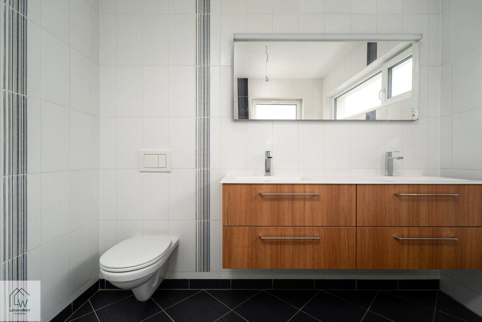 Modernes Badezimmer mit Doppelwaschbecken, Wand-WC und großem Spiegel.
