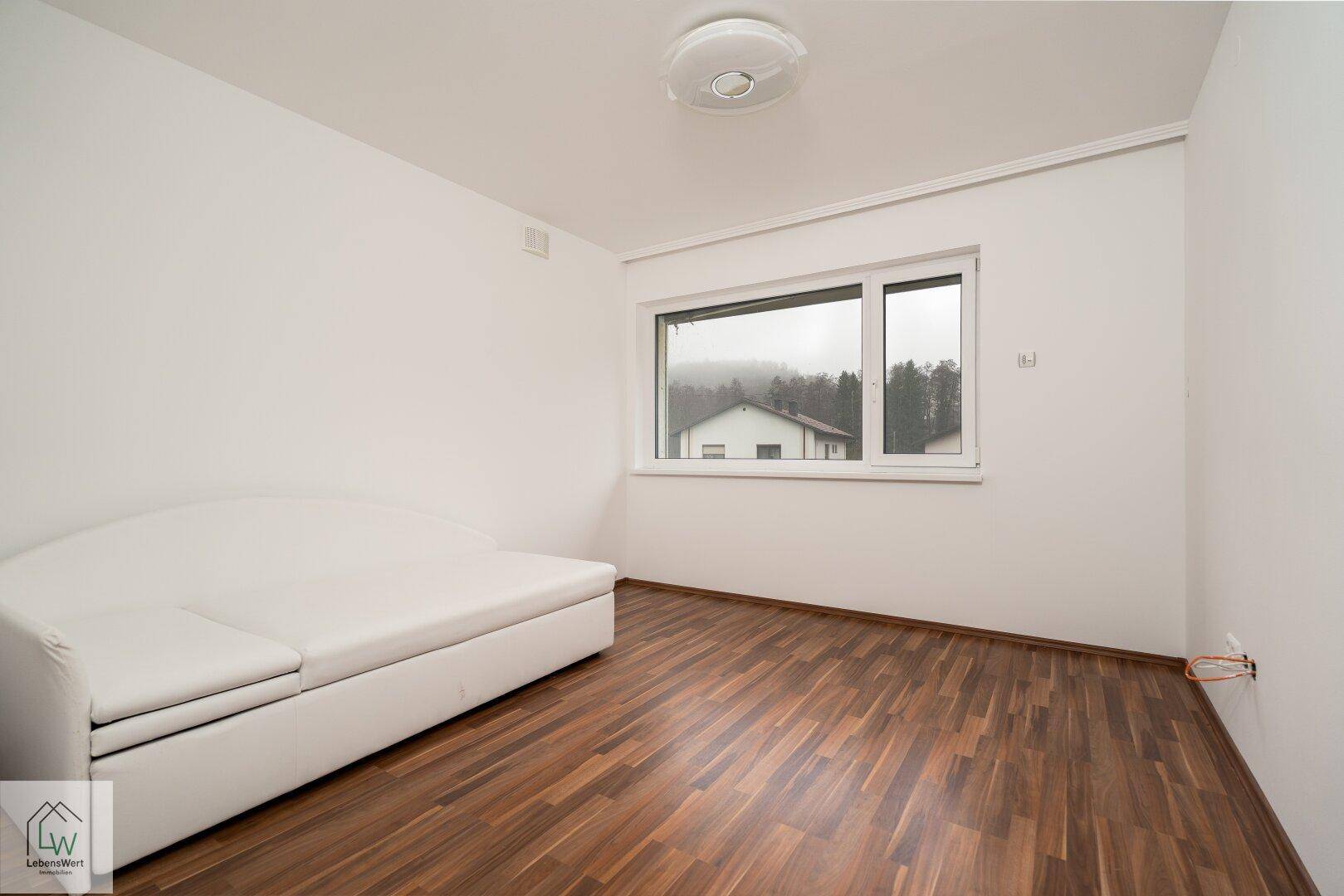 Gemütliches Schlafzimmer mit Laminatboden, Tagesbett und Blick auf die Umgebung.