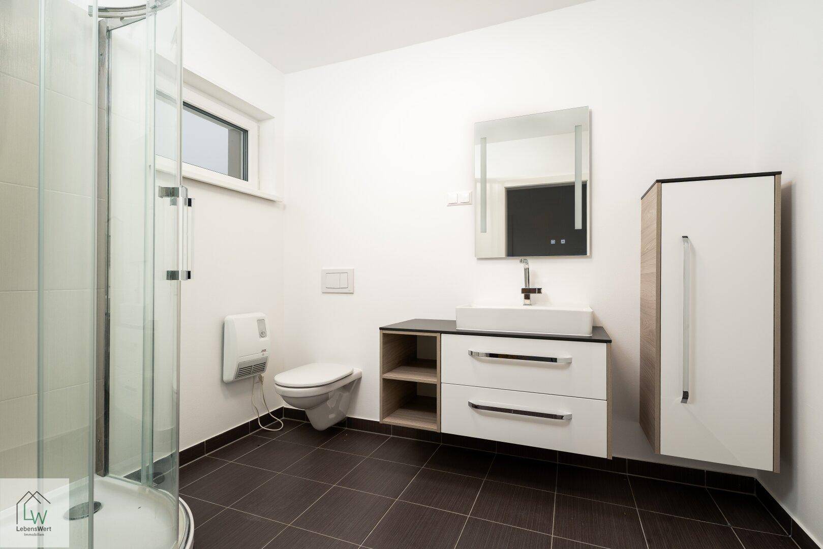 Modernes Badezimmer mit Dusche, WC, Waschbecken und Fenster.