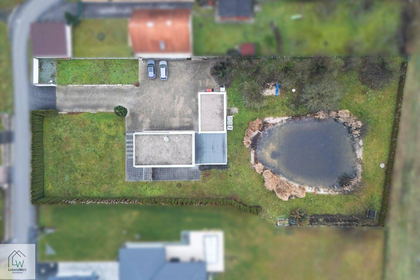 Übersicht des Grundstücks mit modernem Haus, Teich und weitläufigem Gartenbereich.
