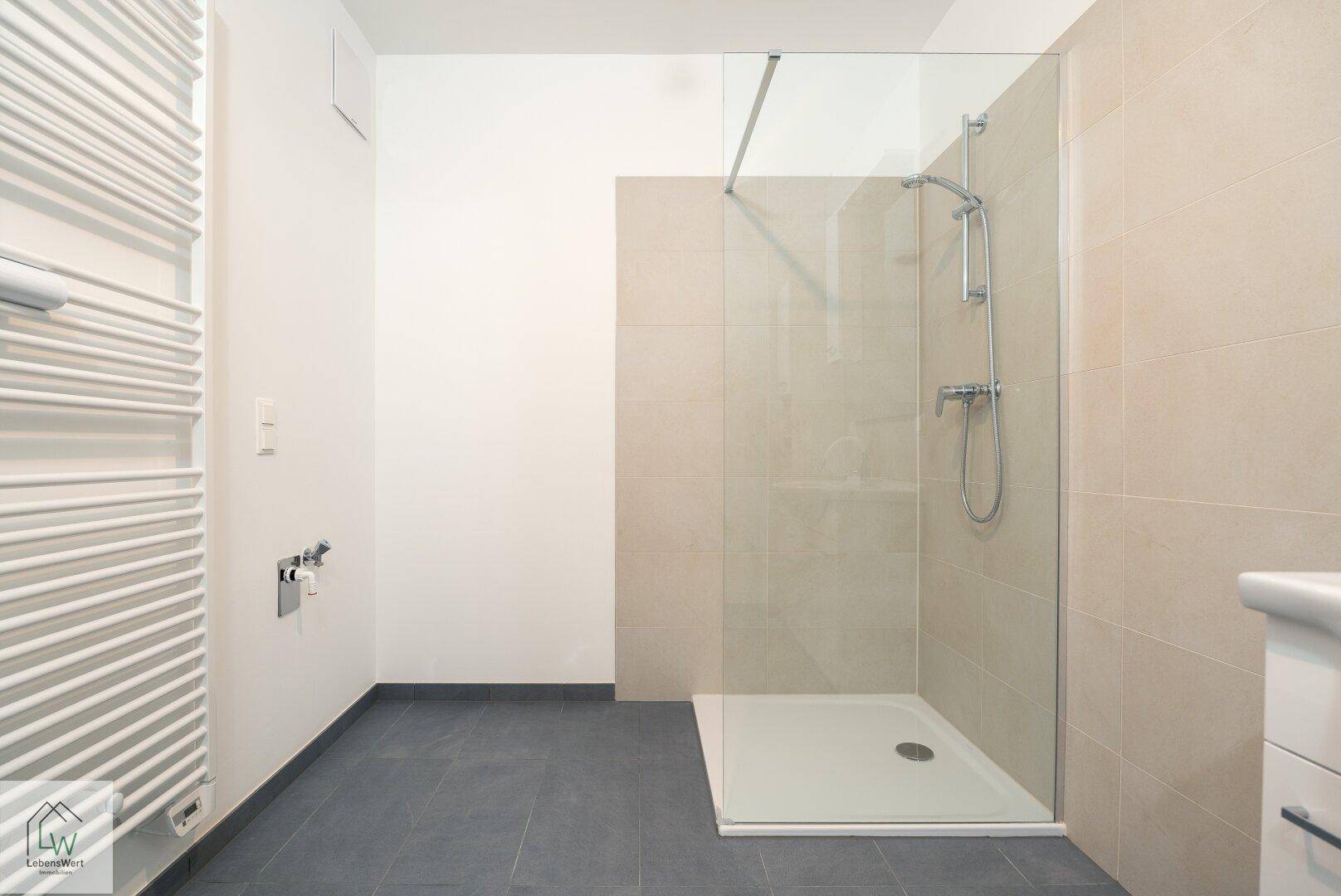 Geräumige, ebenerdige Dusche mit Glasabtrennung und Handtuchheizkörper in modernem Badezimmer.