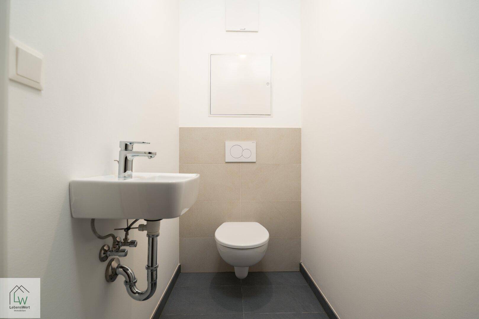 Separates Gäste-WC mit wandhängender Toilette und kleinem Waschbecken.