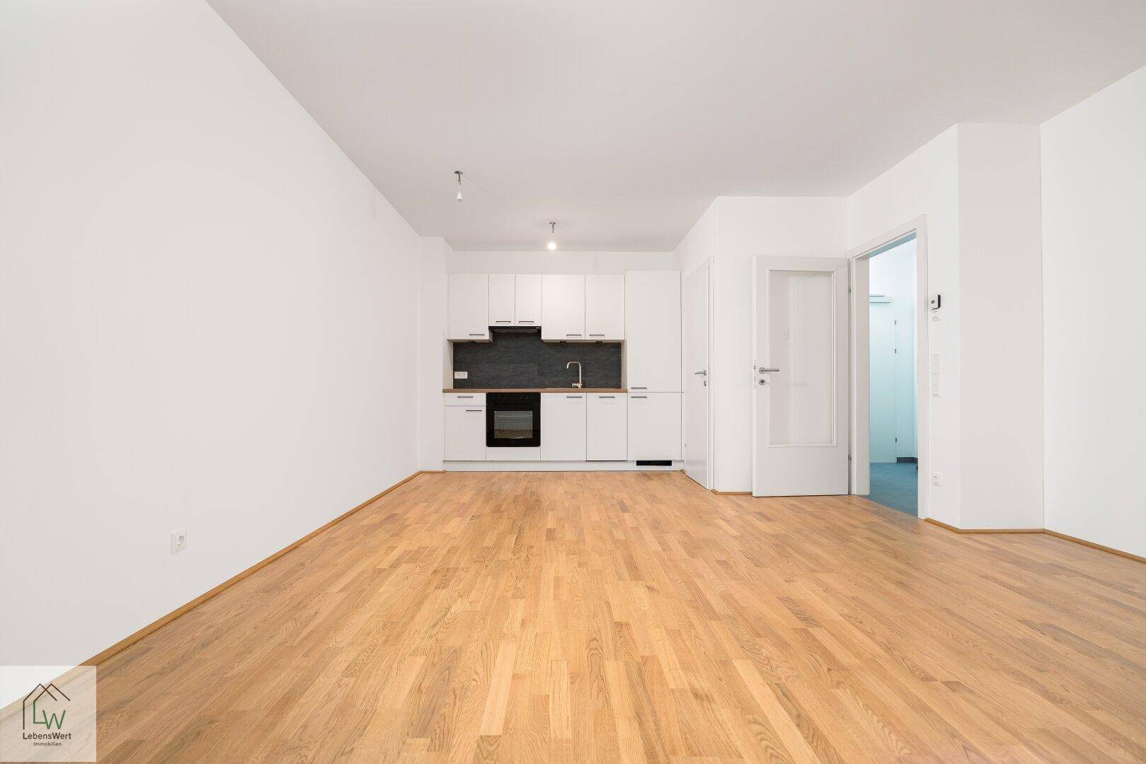 Heller offener Wohnbereich mit integrierter Küche und hochwertigem Parkettboden.