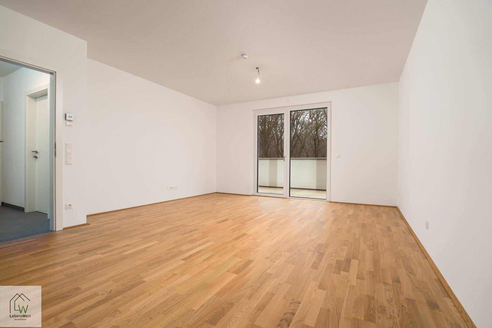 Helles Zimmer mit Parkettboden und Zugang zu einem Balkon, ideal für Wohn- oder Schlafbereich.