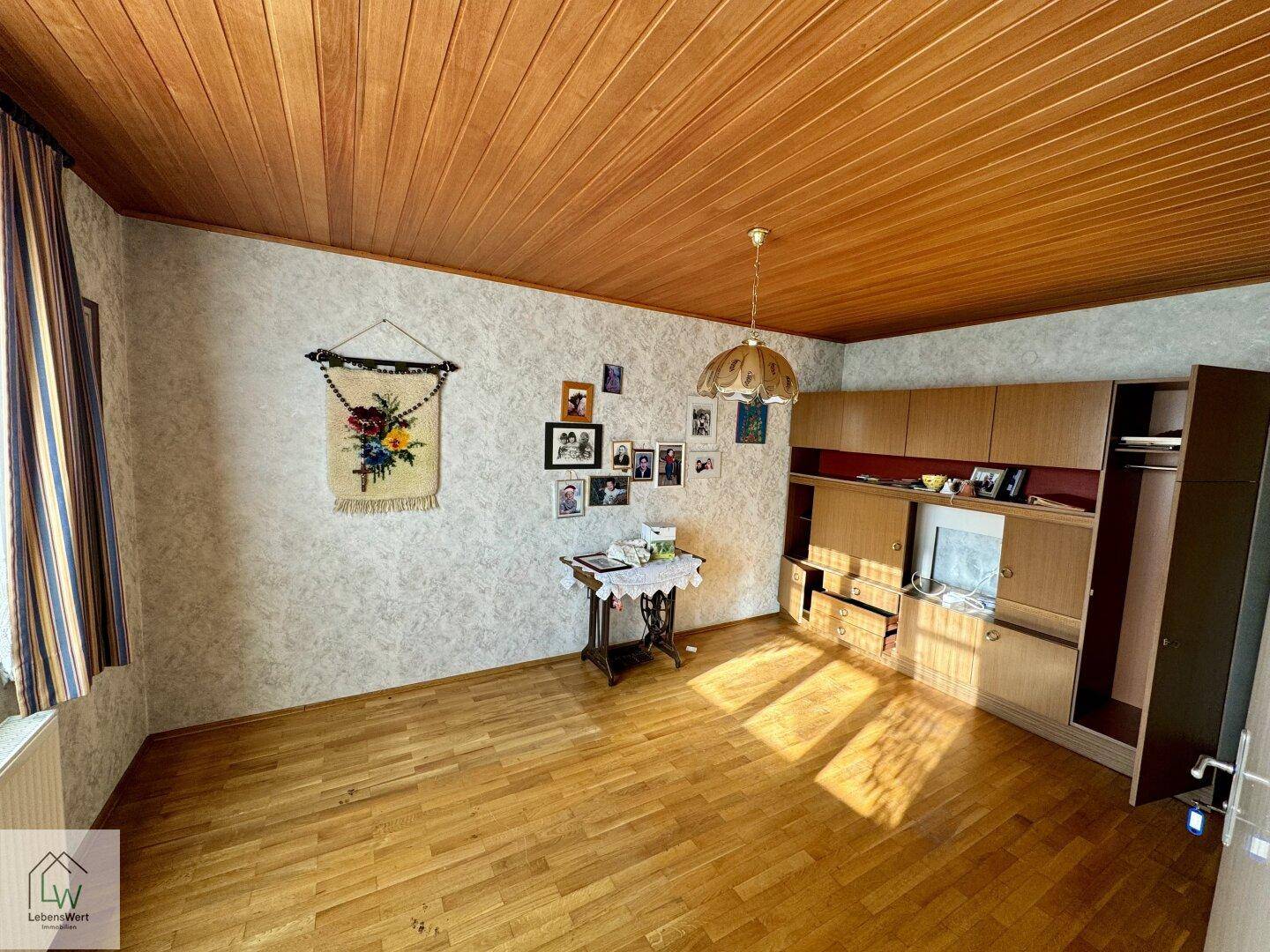 Geräumiges Wohnzimmer mit Holzdecke, Parkettboden und traditioneller Tapete.