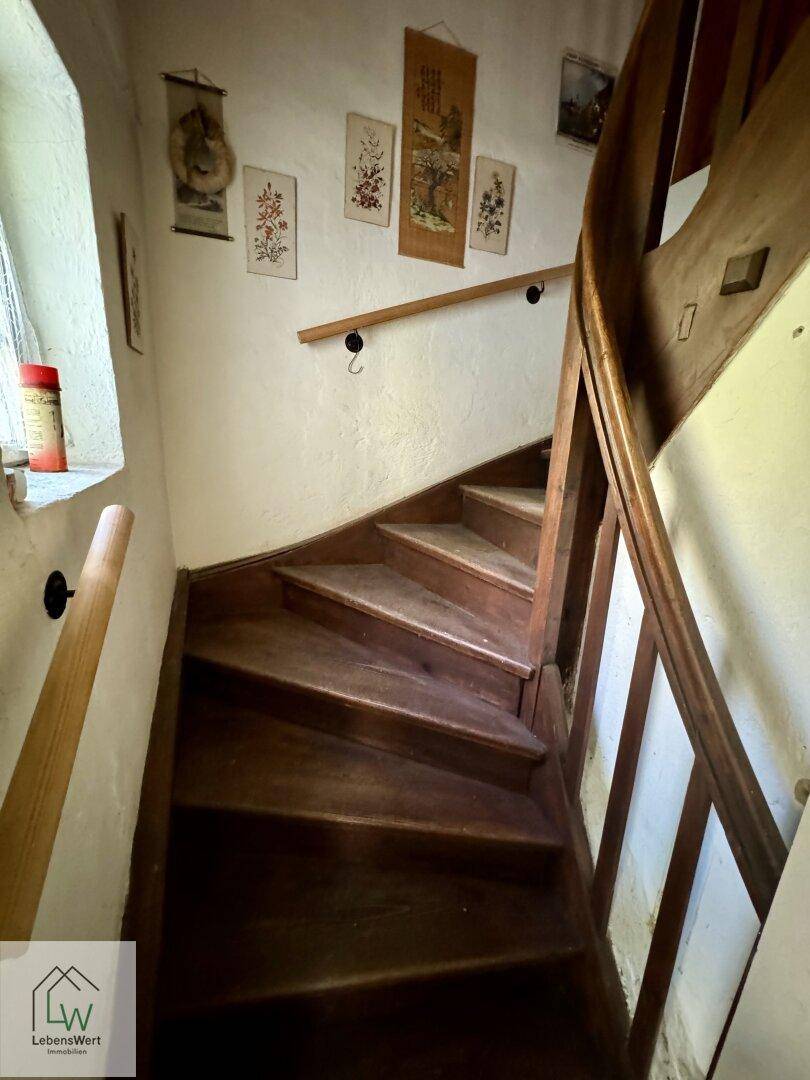 Rustikale Holztreppe mit Handlauf in einem älteren Haus, die in die oberen Stockwerke führt.
