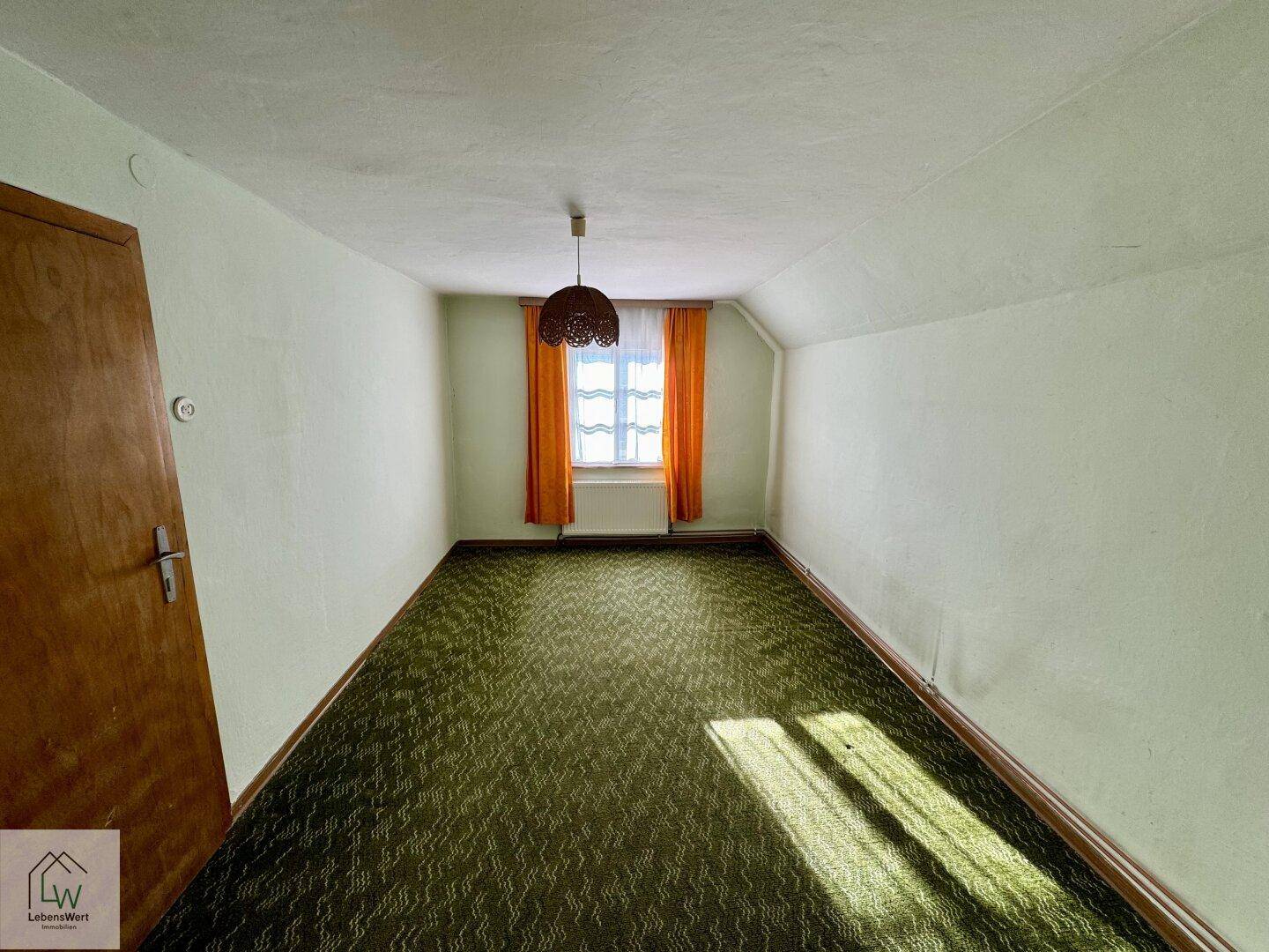 Schlafzimmer mit grüner Teppichboden, Dachschräge und einem Fenster mit orangefarbenen Vorhängen.