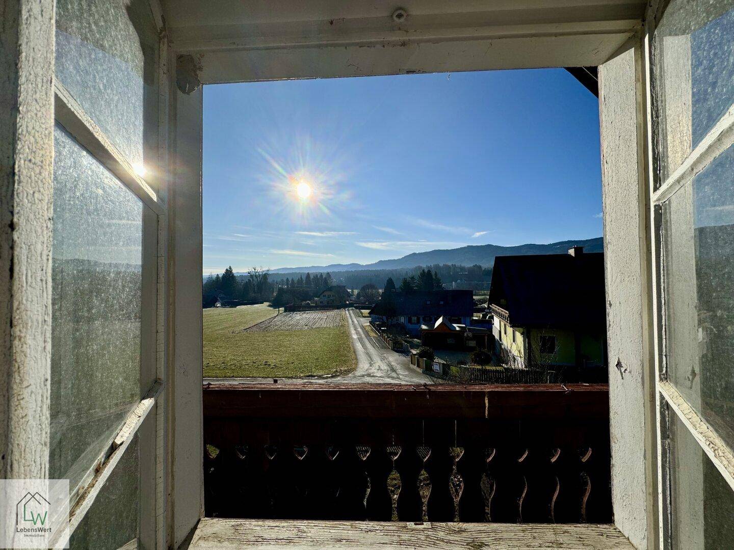 Sonniger Ausblick vom Balkon über die weite Landschaft und die umliegenden Häuser.