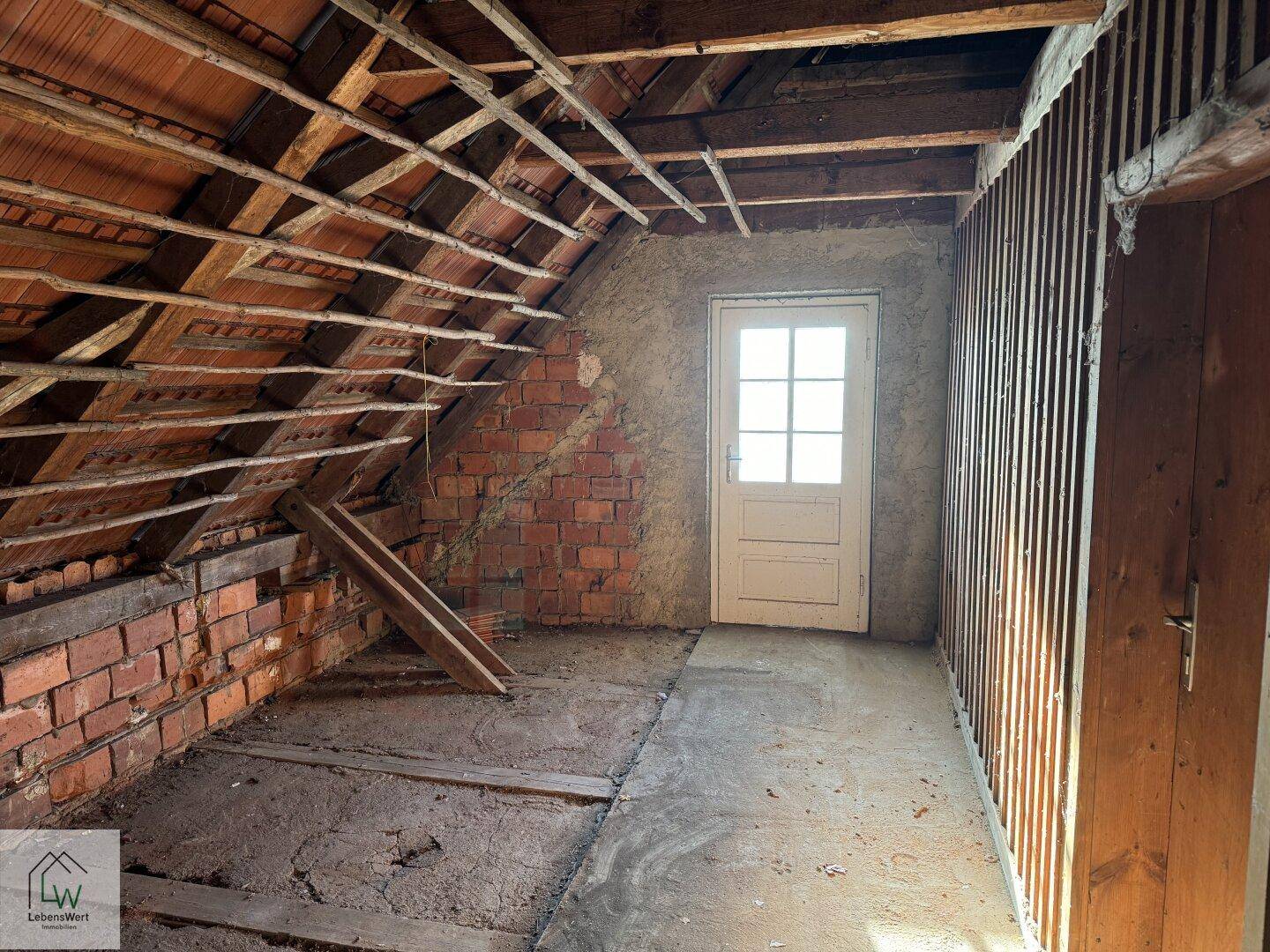 Unausgebauter Dachboden mit sichtbaren Holzbalken und Ziegelwänden, bereit für den Ausbau.