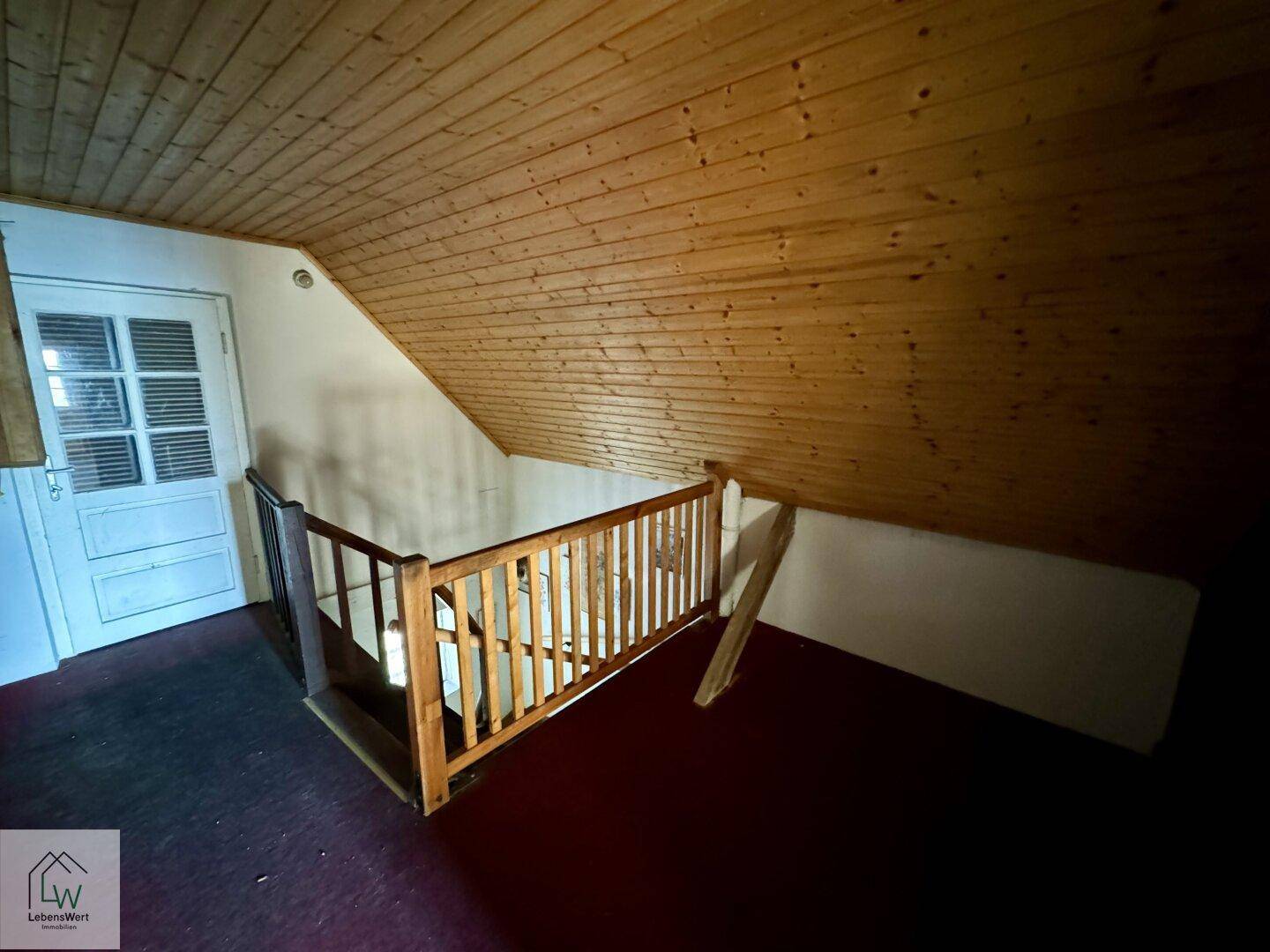 Dachgeschossflur mit Holzvertäfelung an Decke und Schräge sowie einer einfachen Holztreppe.