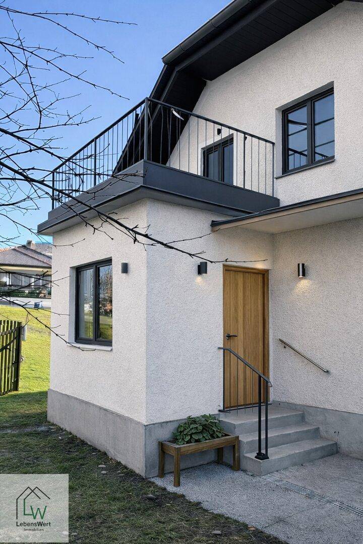 Modernisiertes Haus mit weißer Fassade, Holztür und kleinem Balkon im oberen Stockwerk.
